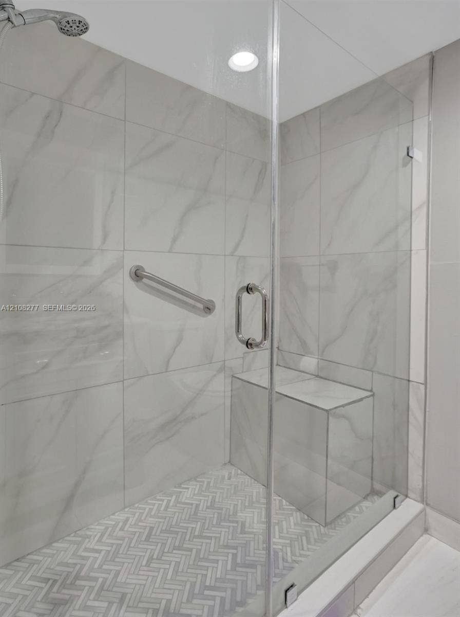 7466 Ashmont Circle, #303, Tamarac, FL 33321 Walk-in shower featuring large-format porcelain wall tile, herringbone-patterned floor tile, frameless glass enclosure, built-in tile bench, and polished chrome hardware