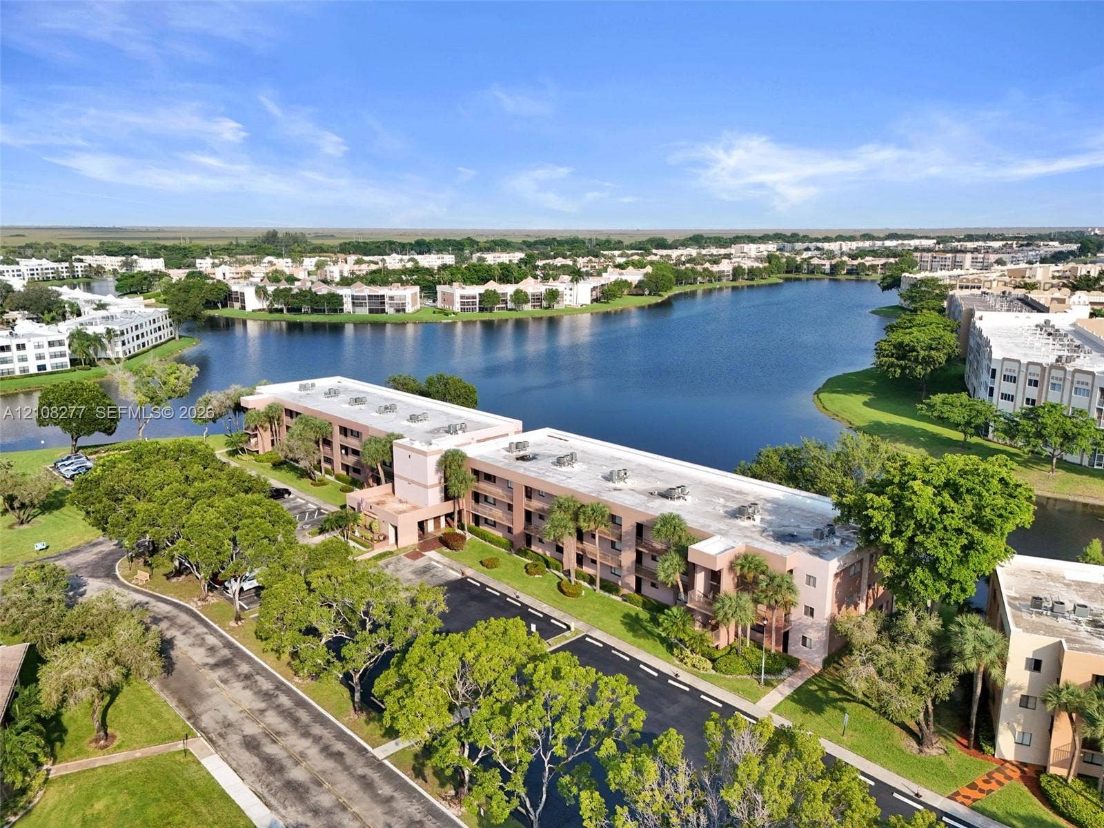 7466 Ashmont Circle, #303, Tamarac, FL 33321 Aerial perspective of a multi-story residential building featuring a flat roofline, paved parking area, mature landscaping, and an expansive waterfront setting