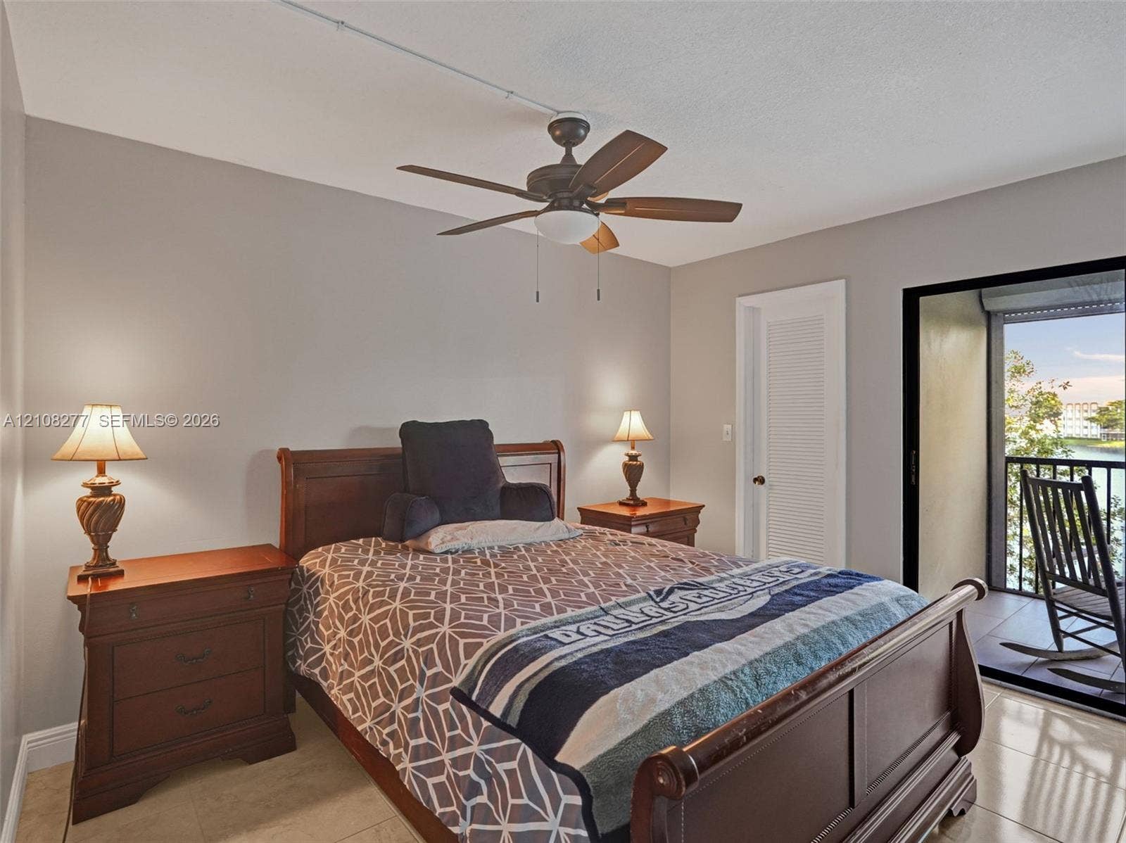 7466 Ashmont Circle, #303, Tamarac, FL 33321 Neutral-toned interior space featuring light-colored tile flooring, a multi-blade ceiling fan, and a louvered closet door with a sliding glass door providing access to a covered balcony