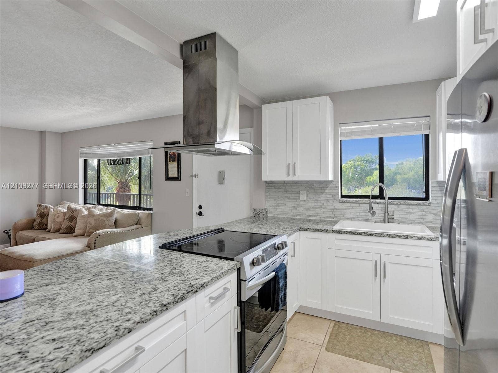 7466 Ashmont Circle, #303, Tamarac, FL 33321 Kitchen featuring white shaker-style cabinetry, stone countertops, stainless steel range with a wall-mounted chimney hood, tiled backsplash, and an undermount sink
