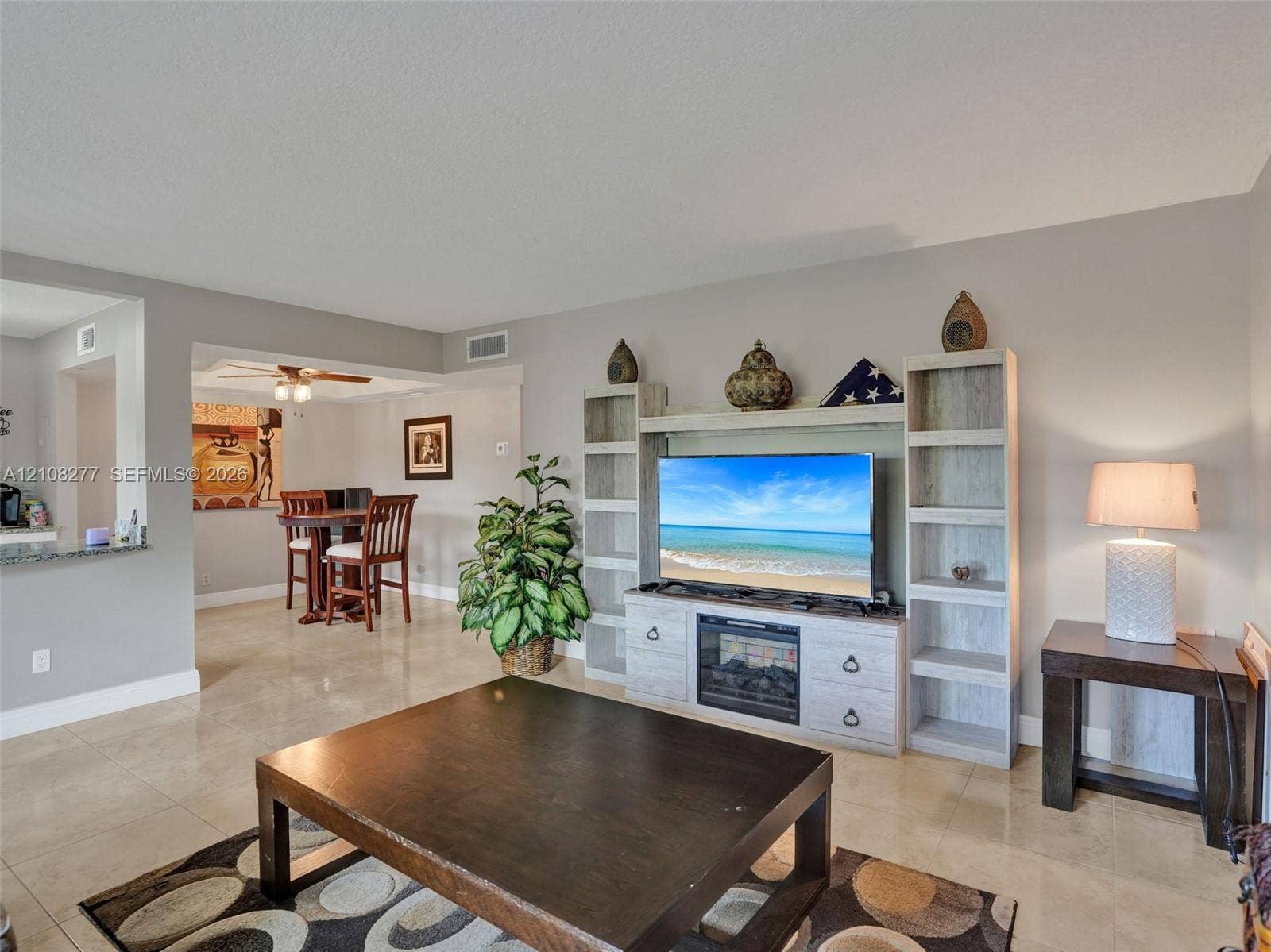 7466 Ashmont Circle, #303, Tamarac, FL 33321 Neutral-toned tile flooring throughout an open living area featuring a custom built-in entertainment center with integrated shelving and an electric fireplace insert