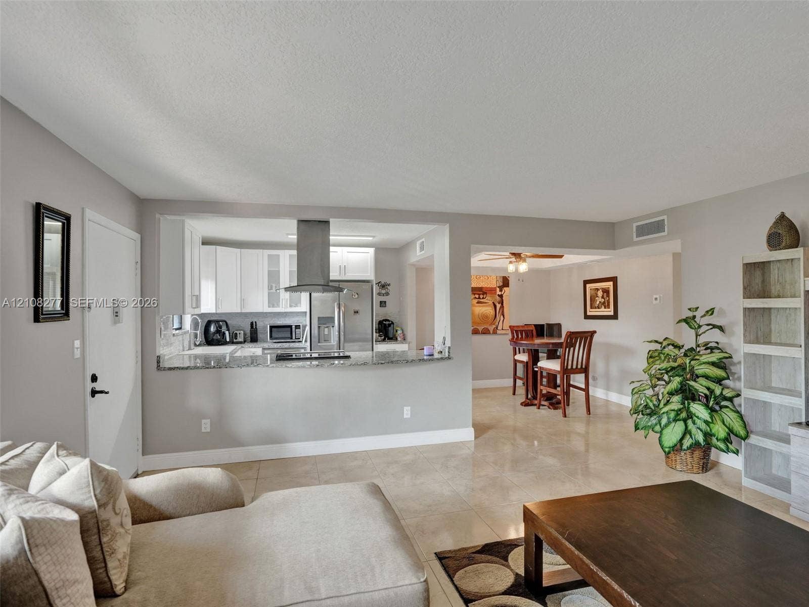 7466 Ashmont Circle, #303, Tamarac, FL 33321 Kitchen featuring white cabinetry, stone-finish countertops, and a stainless steel range hood, complemented by large-format tile flooring throughout