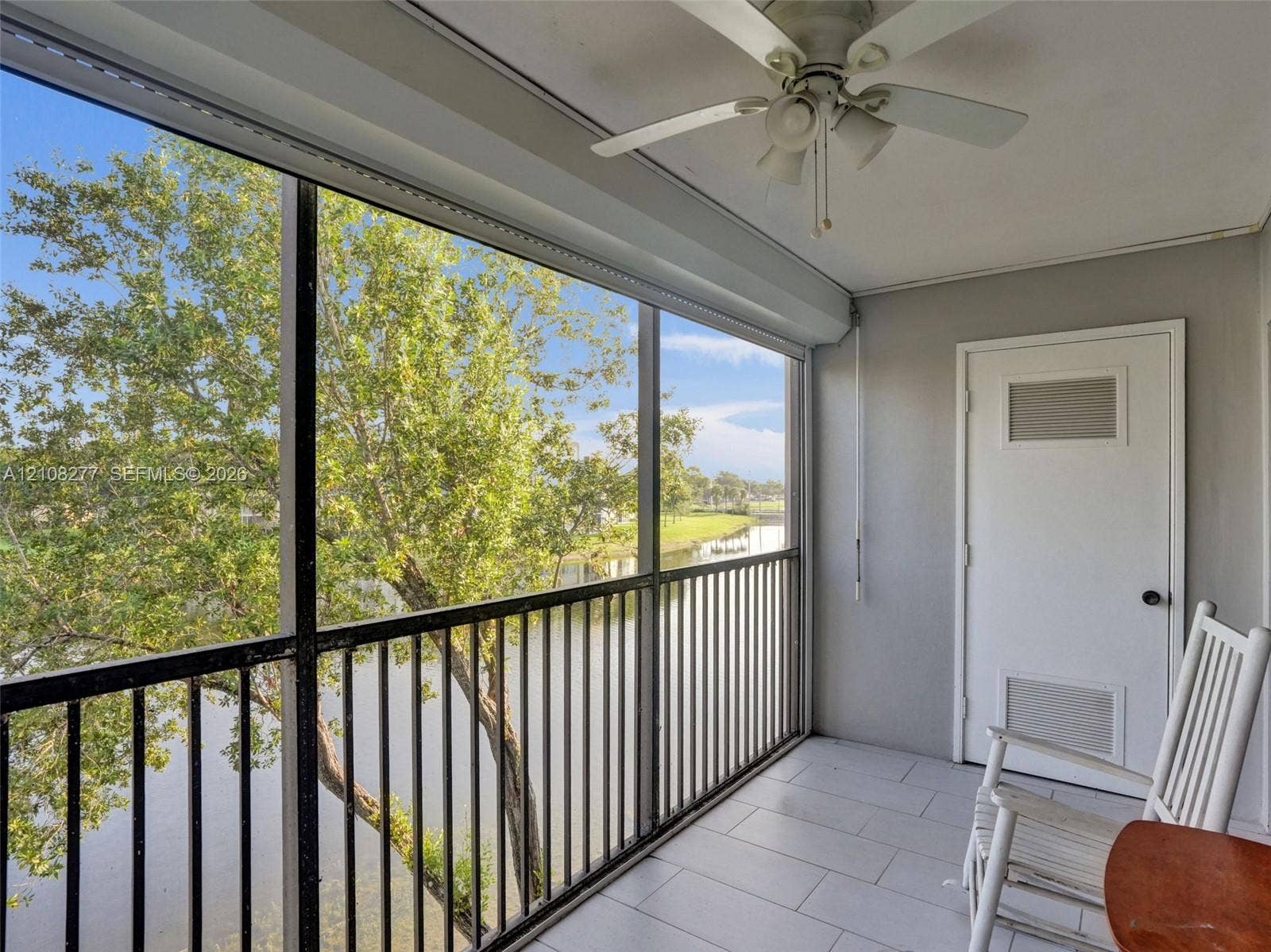 7466 Ashmont Circle, #303, Tamarac, FL 33321 Screened-in balcony featuring tile flooring, a ceiling fan, and metal railings overlooking a water feature