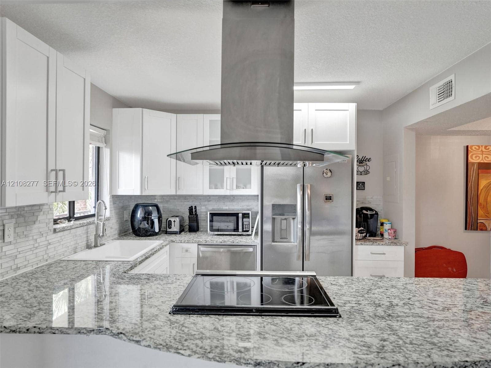 7466 Ashmont Circle, #303, Tamarac, FL 33321 Kitchen featuring stone-finish countertops, stainless steel appliances, a glass and stainless steel island-mounted range hood, shaker-style cabinetry, and a stacked-tile backsplash