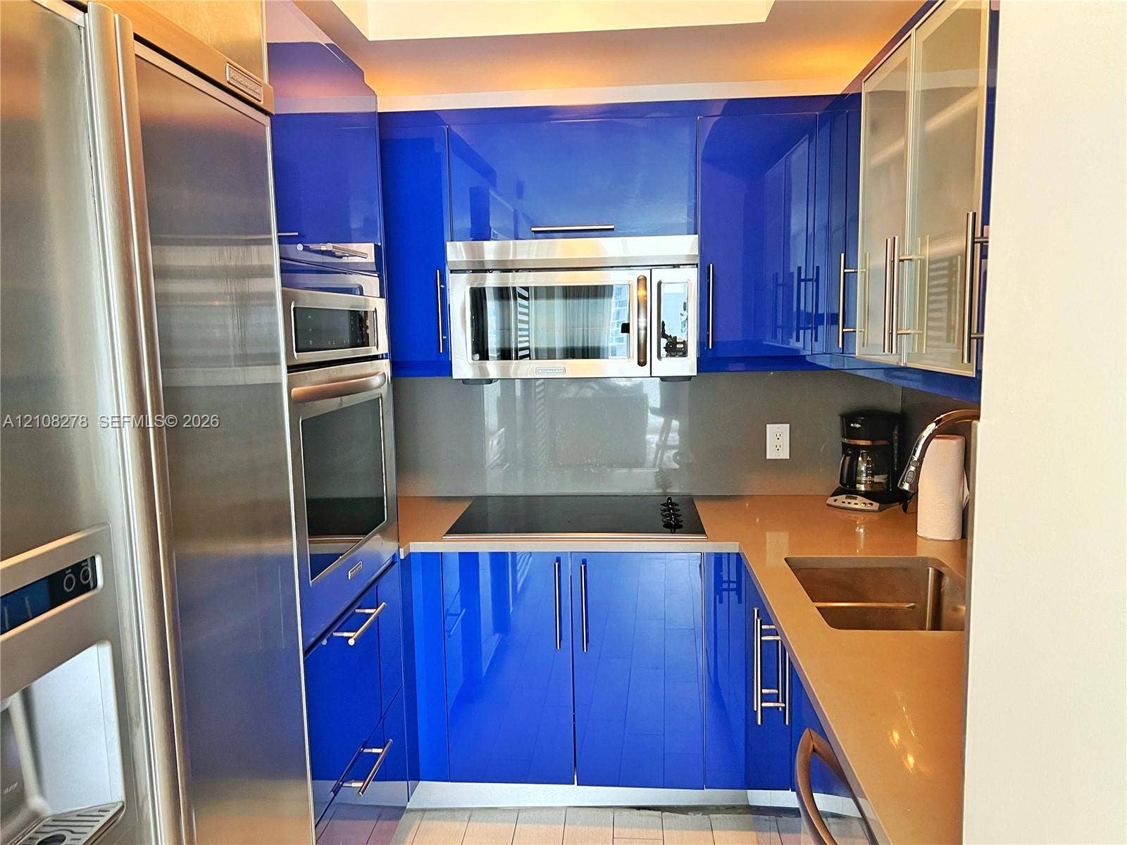 3101 Bayshore Drive, #701, Fort Lauderdale, FL 33304 High-gloss blue cabinetry with integrated hardware, neutral solid-surface countertops, stainless steel wall-mounted oven and microwave, professional-grade refrigerator, and a stainless steel undermount sink