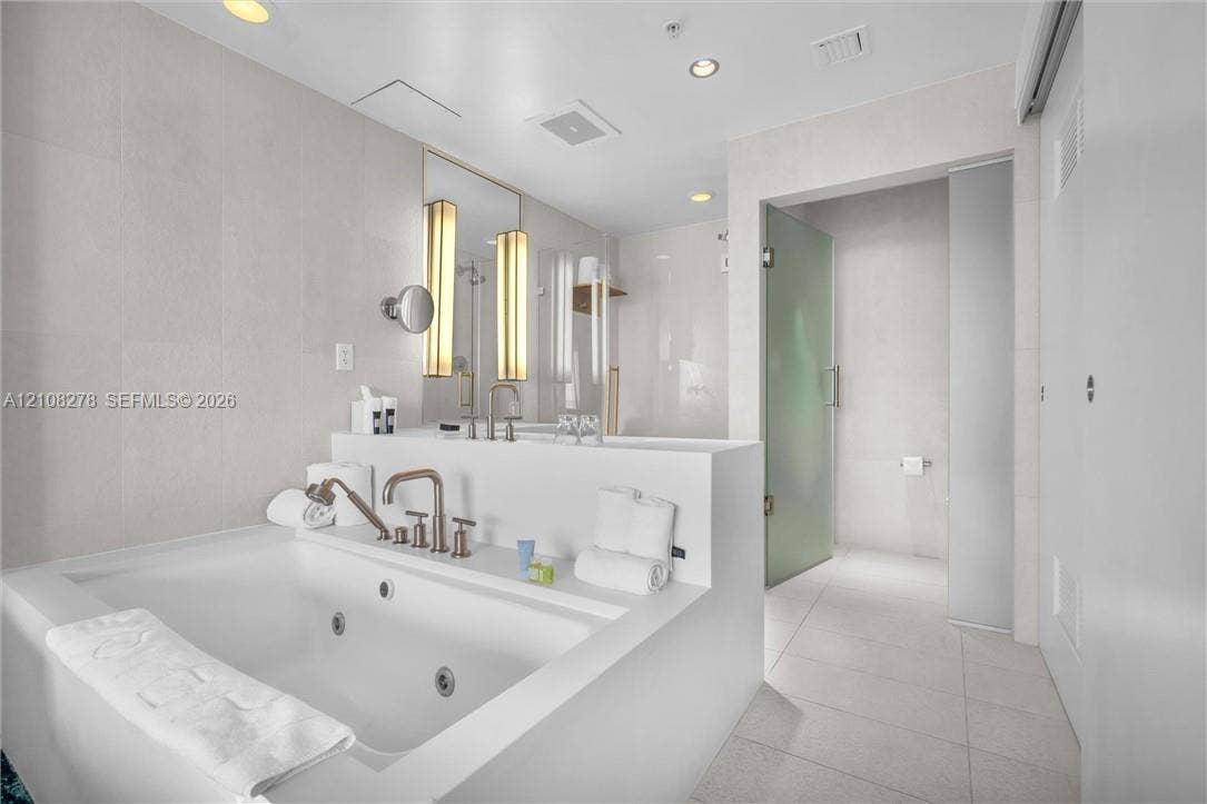 3101 Bayshore Drive, #701, Fort Lauderdale, FL 33304 Jetted soaking tub with deck-mounted metallic fixtures, large-format tile wall surround, dual integrated vanity sinks with sconce lighting, and a walk-in glass-enclosed shower
