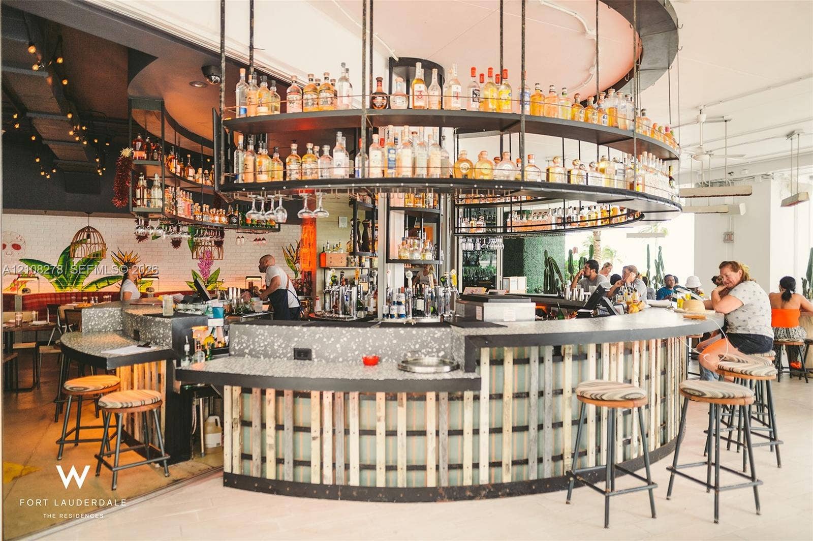 3101 Bayshore Drive, #701, Fort Lauderdale, FL 33304 Circular bar featuring a speckled composite countertop, vertical wood-slat paneling, and an overhead tiered metal shelving system