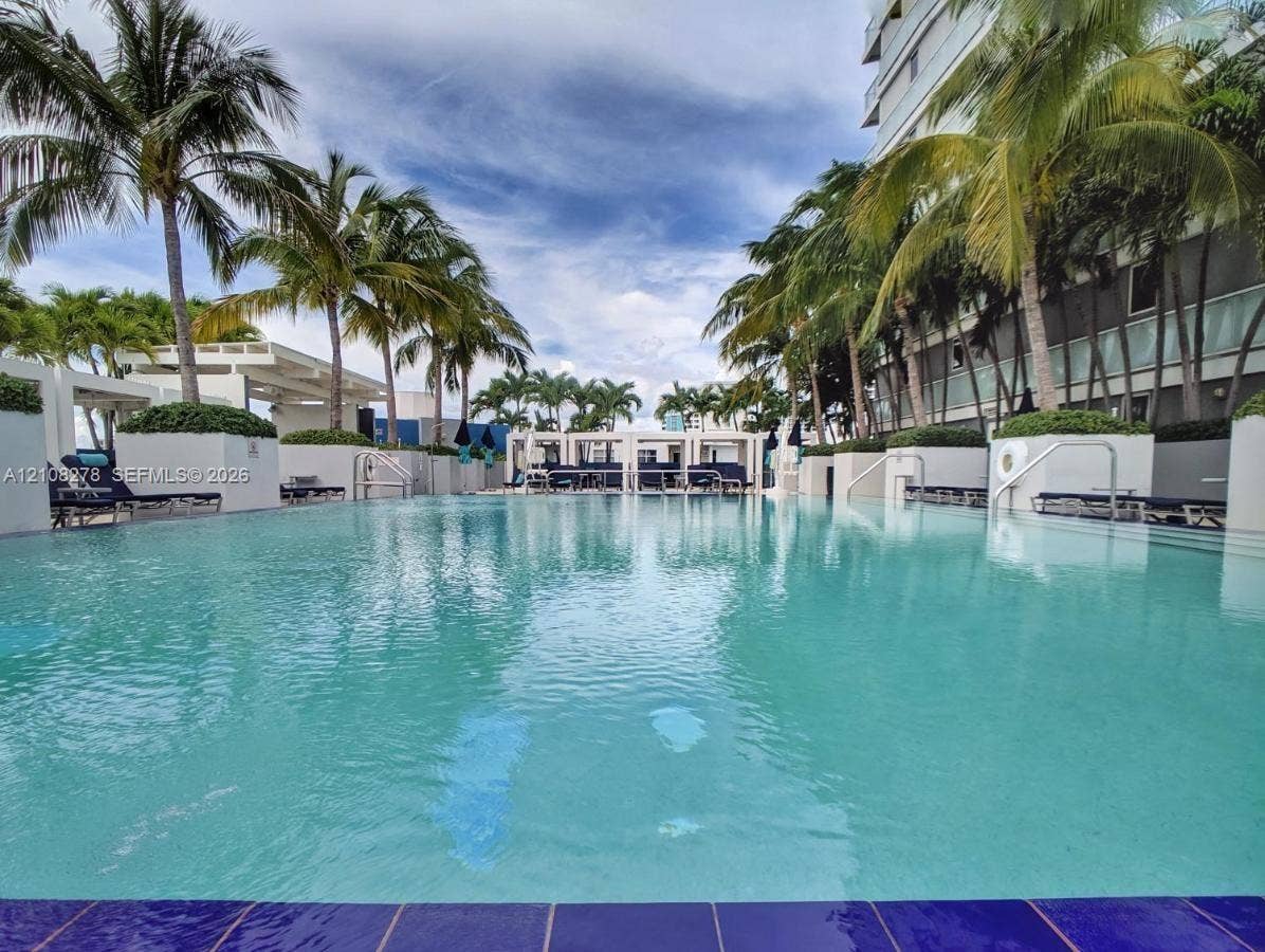 3101 Bayshore Drive, #701, Fort Lauderdale, FL 33304 Swimming pool with tiled perimeter, featuring cabanas, concrete partitions, and mature palm trees