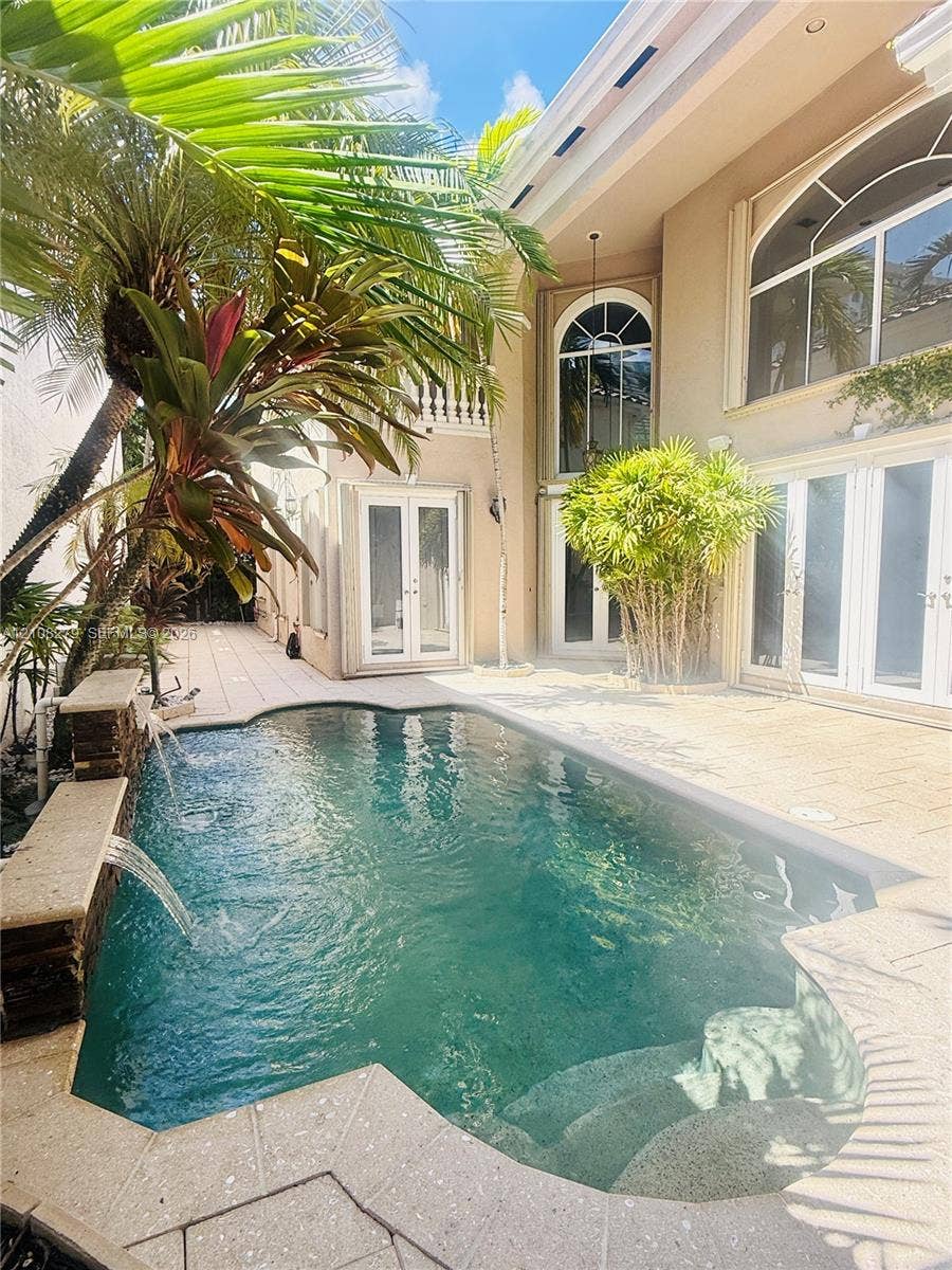 19424 39th Avenue, Sunny Isles Beach, Sunny Isles Beach, FL 33160 Exterior courtyard featuring a custom swimming pool with integrated water features, stone paver decking, multiple arched glass entryways, and two-story stucco architecture