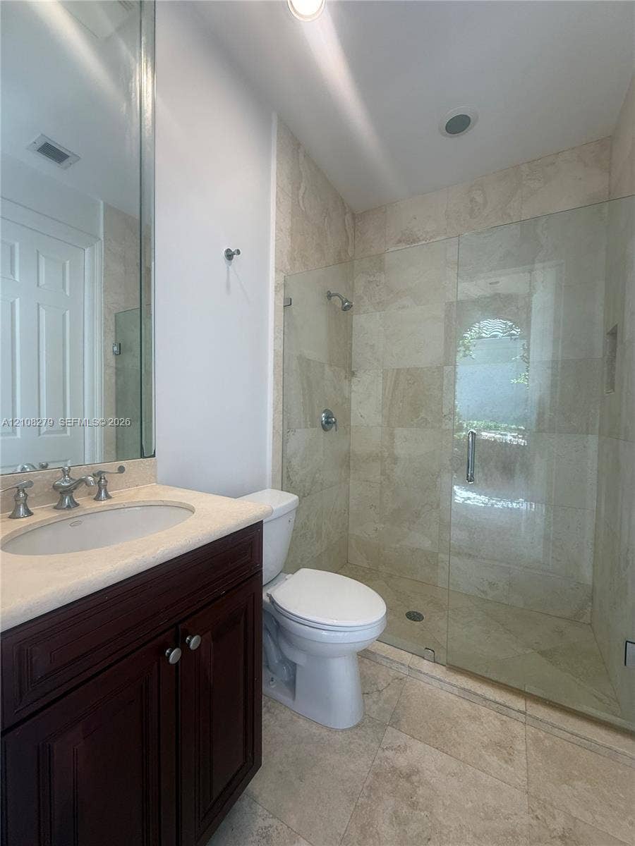 19424 39th Avenue, Sunny Isles Beach, Sunny Isles Beach, FL 33160 Dark wood-finish vanity with a light-toned countertop, undermount sink, and polished metal hardware, paired with a glass-enclosed shower featuring tile walls and matching tile flooring