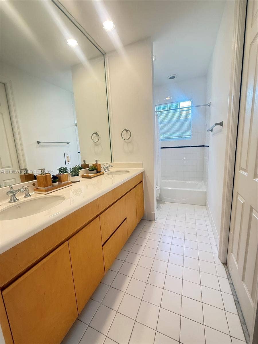 19424 39th Avenue, Sunny Isles Beach, Sunny Isles Beach, FL 33160 Dual-sink vanity with light wood-finish cabinetry, solid surface countertop, expansive wall-mounted mirror, and tile flooring