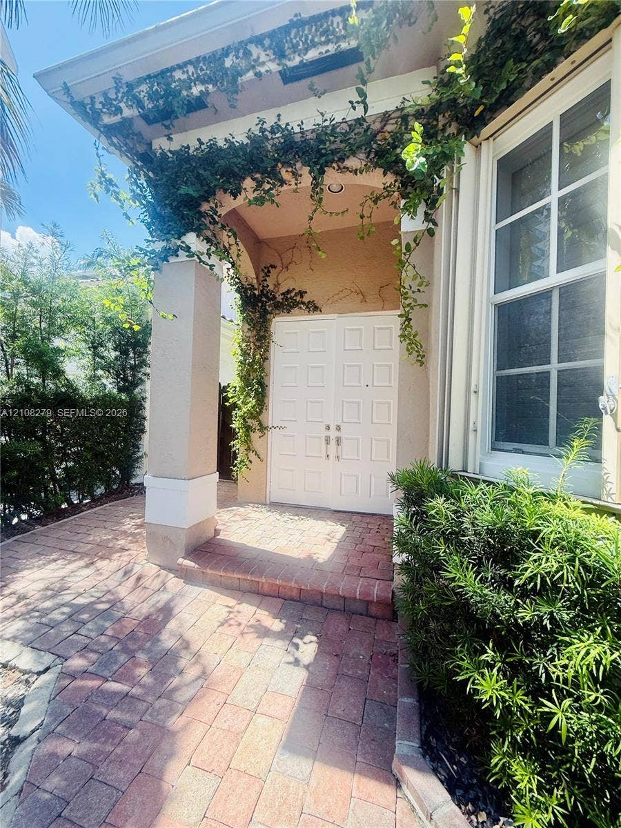19424 39th Avenue, Sunny Isles Beach, Sunny Isles Beach, FL 33160 Covered entryway featuring a brick paver walkway, double doors with paneled detailing, a neutral-toned exterior, and integrated structural columns