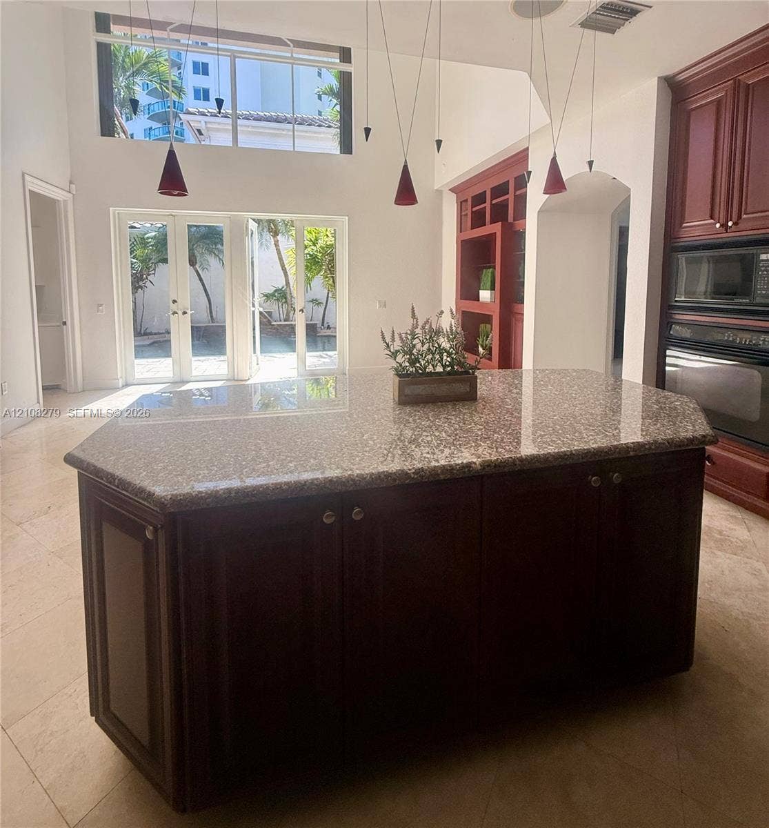 19424 39th Avenue, Sunny Isles Beach, Sunny Isles Beach, FL 33160 Kitchen island with a stone countertop and dark wood-finish cabinetry, vaulted ceilings, multi-light pendant fixture, double wall oven, and French doors featuring transom windows