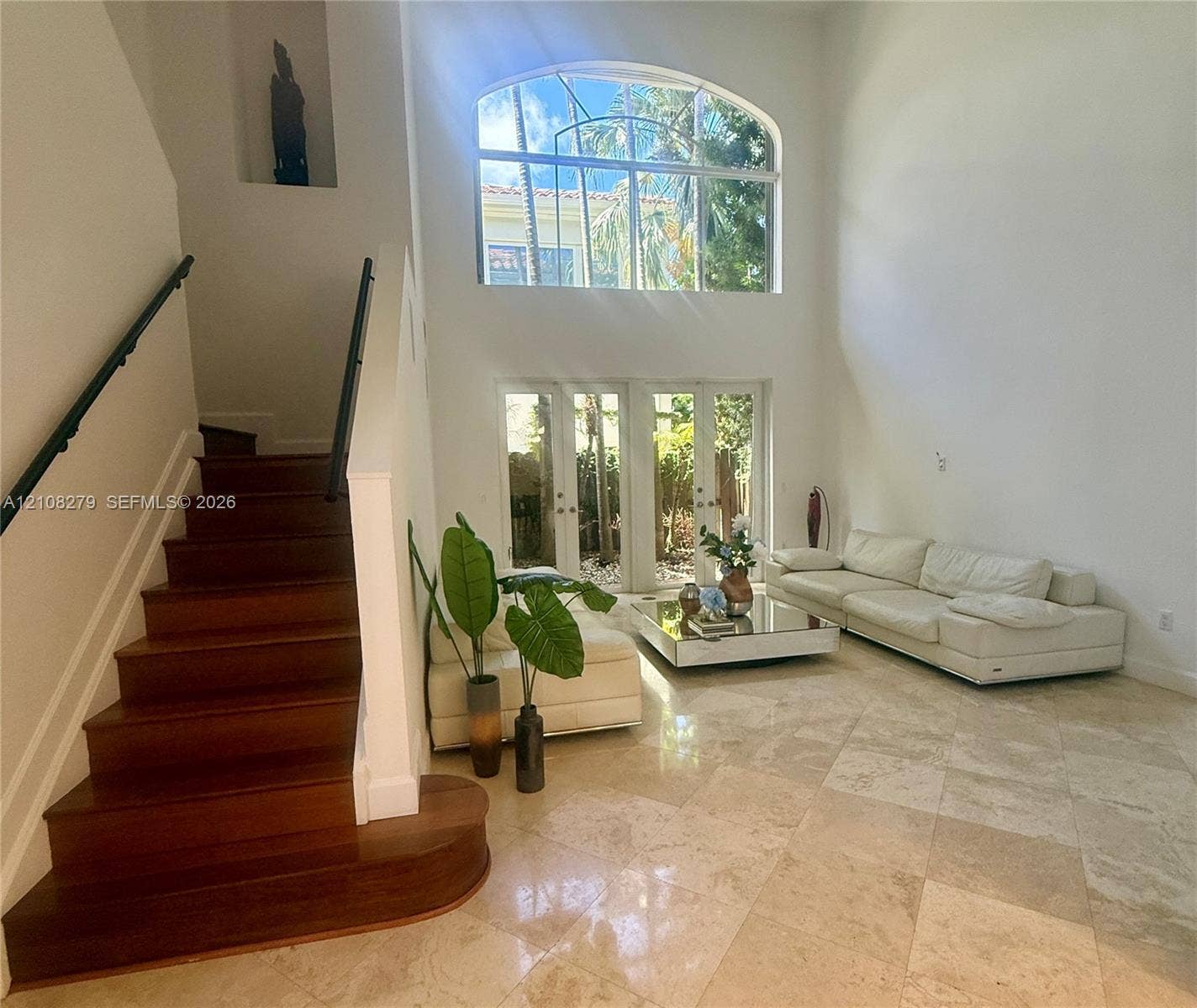 19424 39th Avenue, Sunny Isles Beach, Sunny Isles Beach, FL 33160 High-ceiling interior featuring stone tile flooring, a wood-finish staircase with a wrought-iron handrail, a large arched window, and full-height glass-paned doors