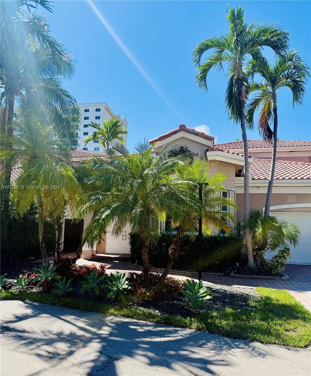 19424 39th Avenue, Sunny Isles Beach, Sunny Isles Beach, FL 33160 Stucco exterior featuring a terracotta tile roof, paver driveway, attached garage, and mature palm landscaping