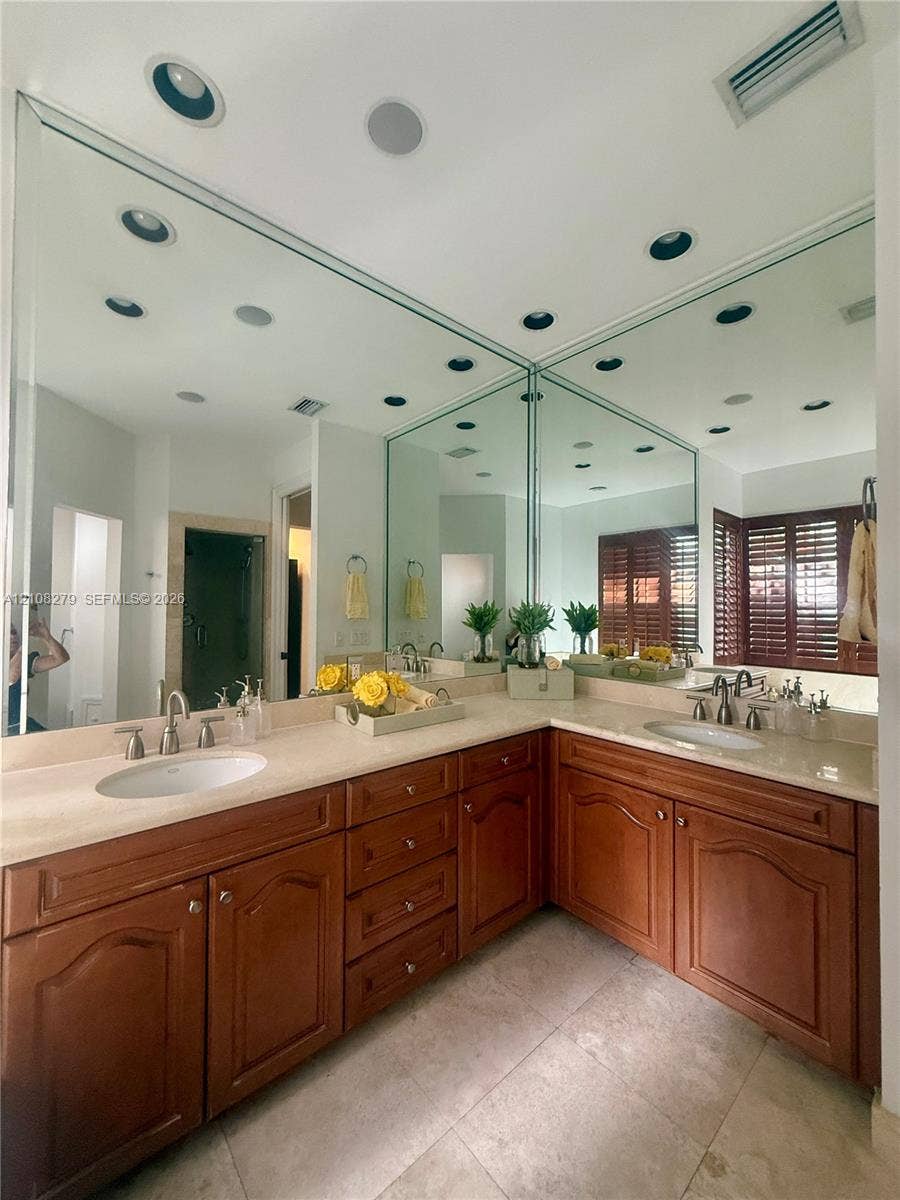 19424 39th Avenue, Sunny Isles Beach, Sunny Isles Beach, FL 33160 L-shaped vanity featuring raised-panel wood cabinetry, light-toned stone-finish countertops, dual integrated undermount sinks, and full-height wall mirrors