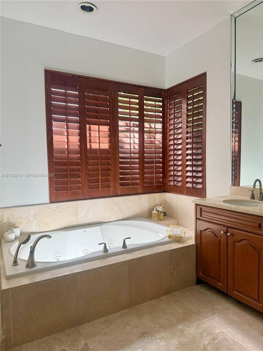 19424 39th Avenue, Sunny Isles Beach, Sunny Isles Beach, FL 33160 Jetted soaking tub with deck-mounted chrome fixtures, custom wood shutters, stone-tiled tub surround, wood vanity cabinetry, and large-format tile flooring