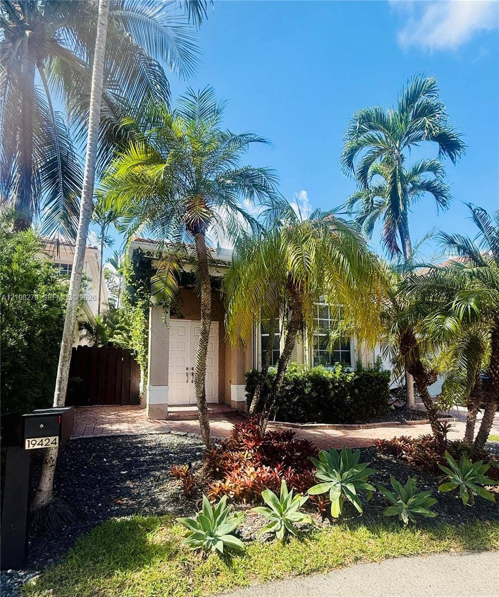 19424 39th Avenue, Sunny Isles Beach, Sunny Isles Beach, FL 33160 Exterior featuring double-door entry, brick-paved walkway, mature palm trees, and established ornamental landscaping