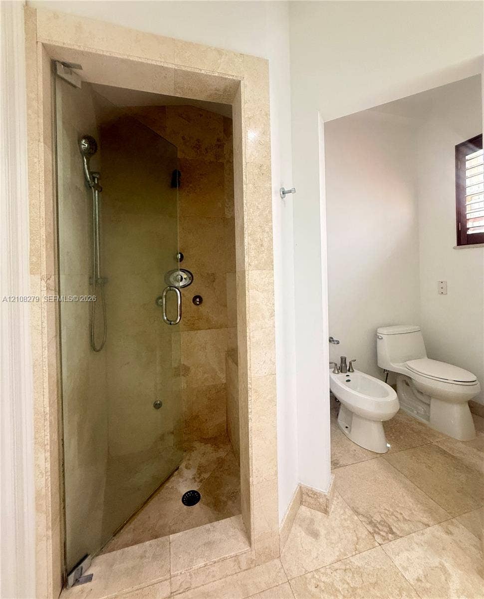19424 39th Avenue, Sunny Isles Beach, Sunny Isles Beach, FL 33160 Walk-in shower featuring a frameless glass door, stone-tile surround, and handheld showerhead, accompanied by a bidet and toilet with stone-tile flooring