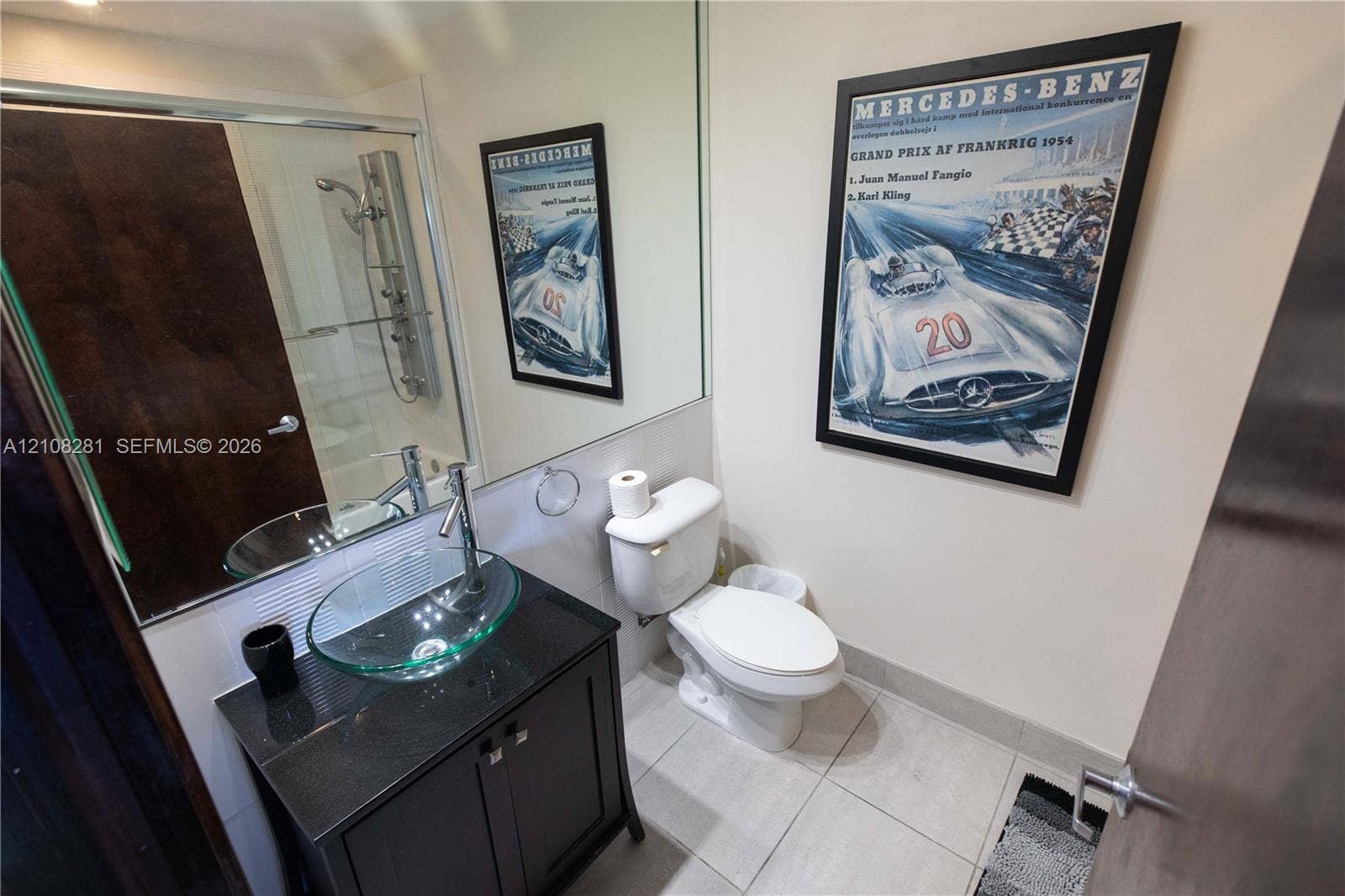 Bathroom featuring a vanity with dark cabinetry, stone-finish countertop, and a glass vessel sink with a chrome faucet, complemented by a floor-to-ceiling mirror and a glass-enclosed shower with a multi-head panel