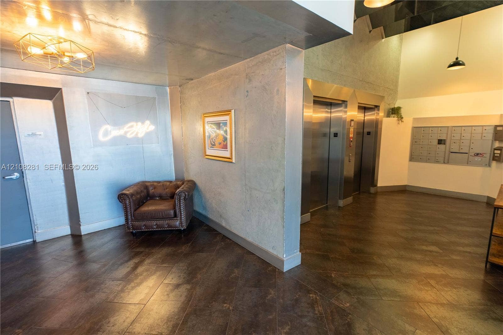Industrial-style lobby featuring polished concrete walls, dark tile flooring in a herringbone pattern, stainless steel elevator doors, and integrated metallic pendant lighting