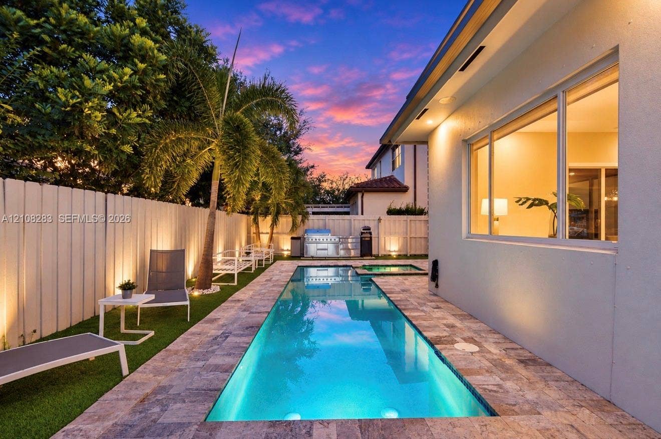 15215 SW 176th Lane, Miami, FL 33187 Rectangular swimming pool featuring a stone-paver surround, integrated spa, built-in outdoor grill station, and artificial turf lawn, enclosed by privacy fencing