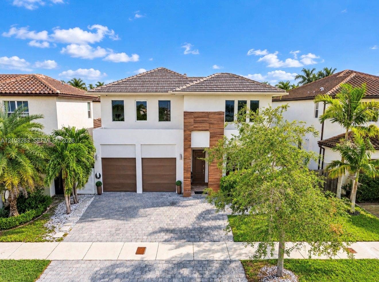 15215 SW 176th Lane, Miami, FL 33187 Two-story exterior featuring a stucco facade, wood-slat vertical accents, a concrete tile roof, dual garage doors, and a paver driveway