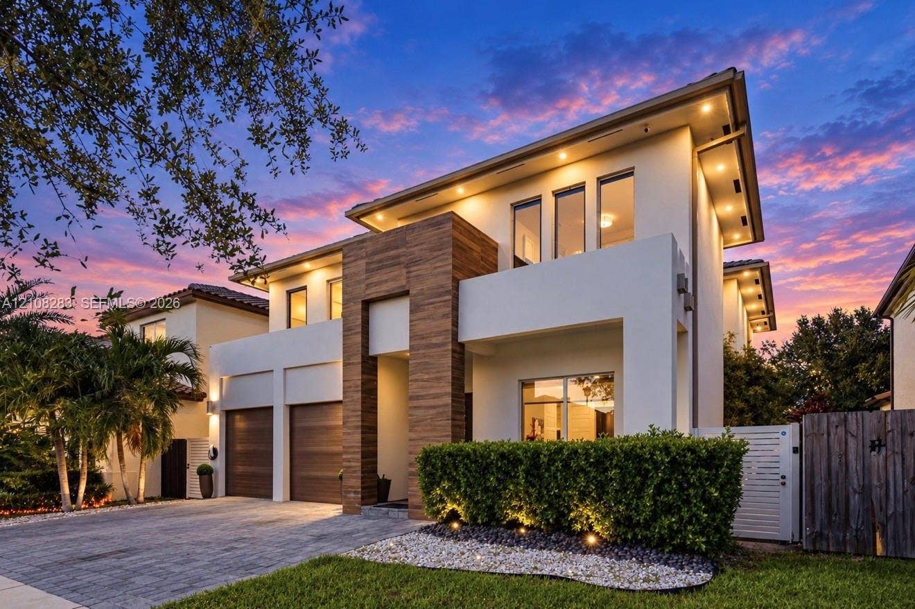 15215 SW 176th Lane, Miami, FL 33187 Contemporary exterior featuring smooth stucco finish, vertical wood-paneling accents, recessed soffit lighting, two-car garage with wood-finish doors, and paved driveway