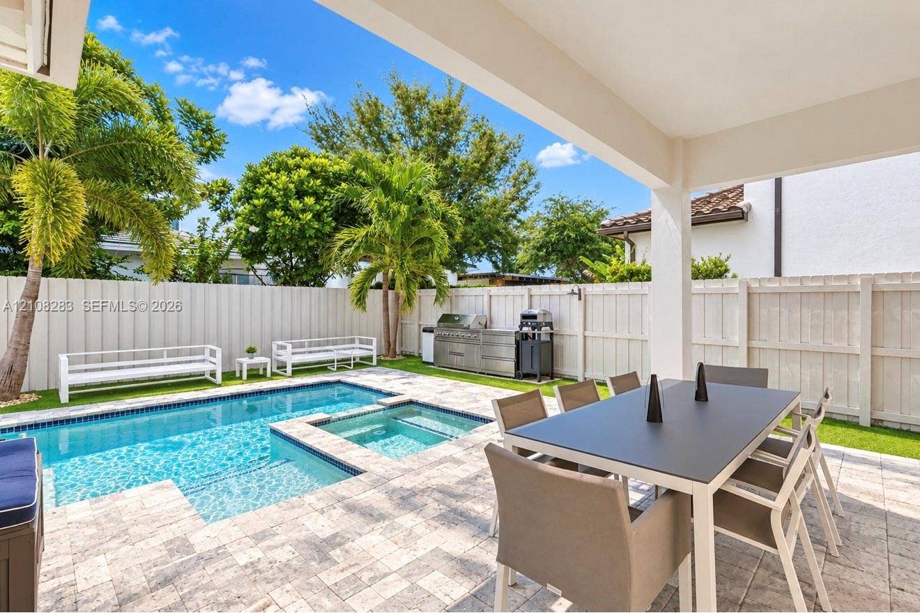 15215 SW 176th Lane, Miami, FL 33187 Covered patio featuring stone-tiled decking, a swimming pool with integrated spa, built-in stainless steel outdoor kitchen, and vinyl privacy fencing
