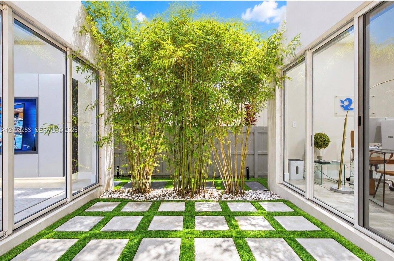 15215 SW 176th Lane, Miami, FL 33187 Interior courtyard featuring floor-to-ceiling glass sliding doors, concrete paver grid, synthetic turf, mature bamboo, and perimeter privacy fencing