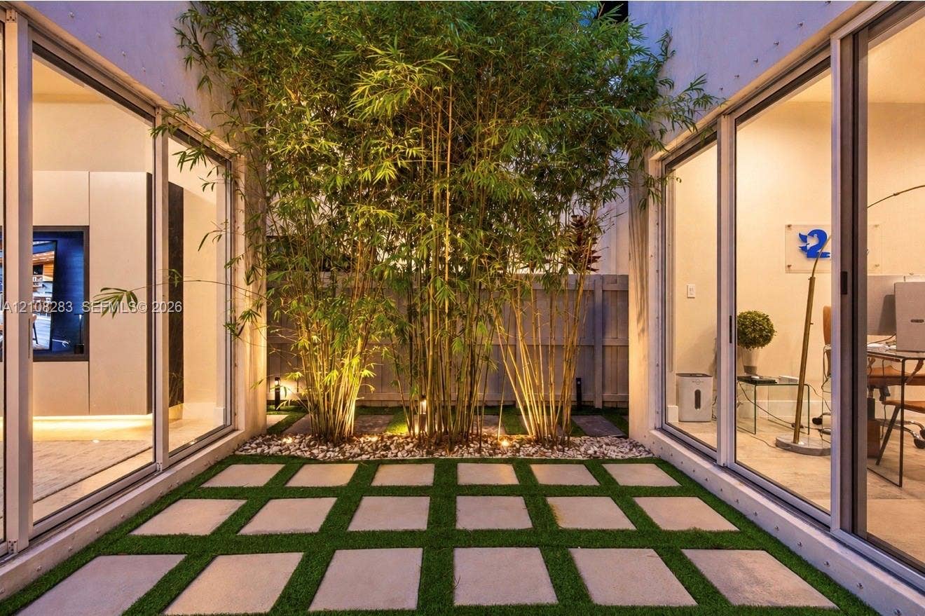15215 SW 176th Lane, Miami, FL 33187 Central atrium featuring large-format concrete pavers, integrated synthetic turf grid, mature bamboo specimens, and expansive floor-to-ceiling sliding glass doors