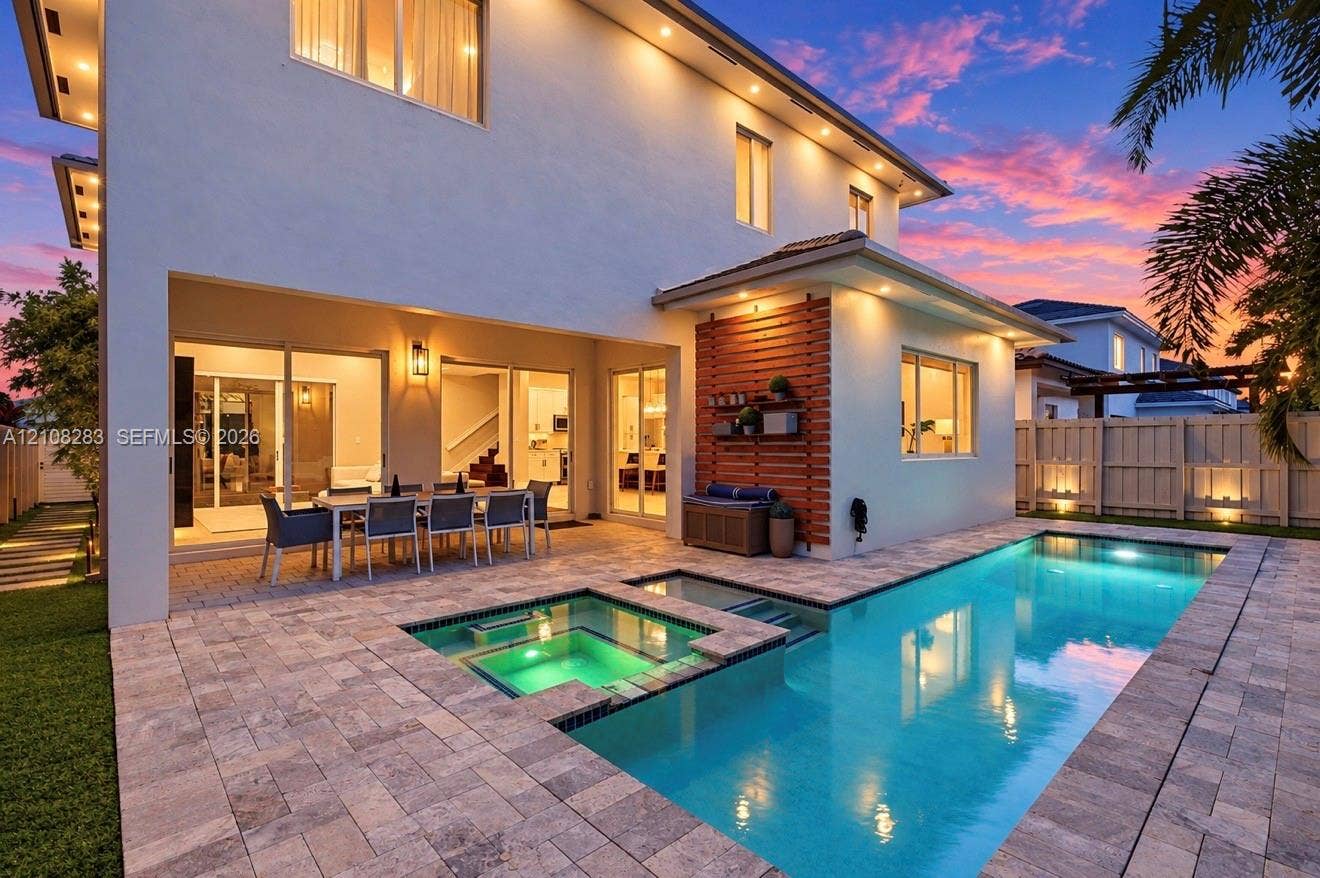 15215 SW 176th Lane, Miami, FL 33187 Rear exterior featuring a covered patio, rectangular swimming pool with integrated spa, stone paver decking, and horizontal wood-slat wall cladding