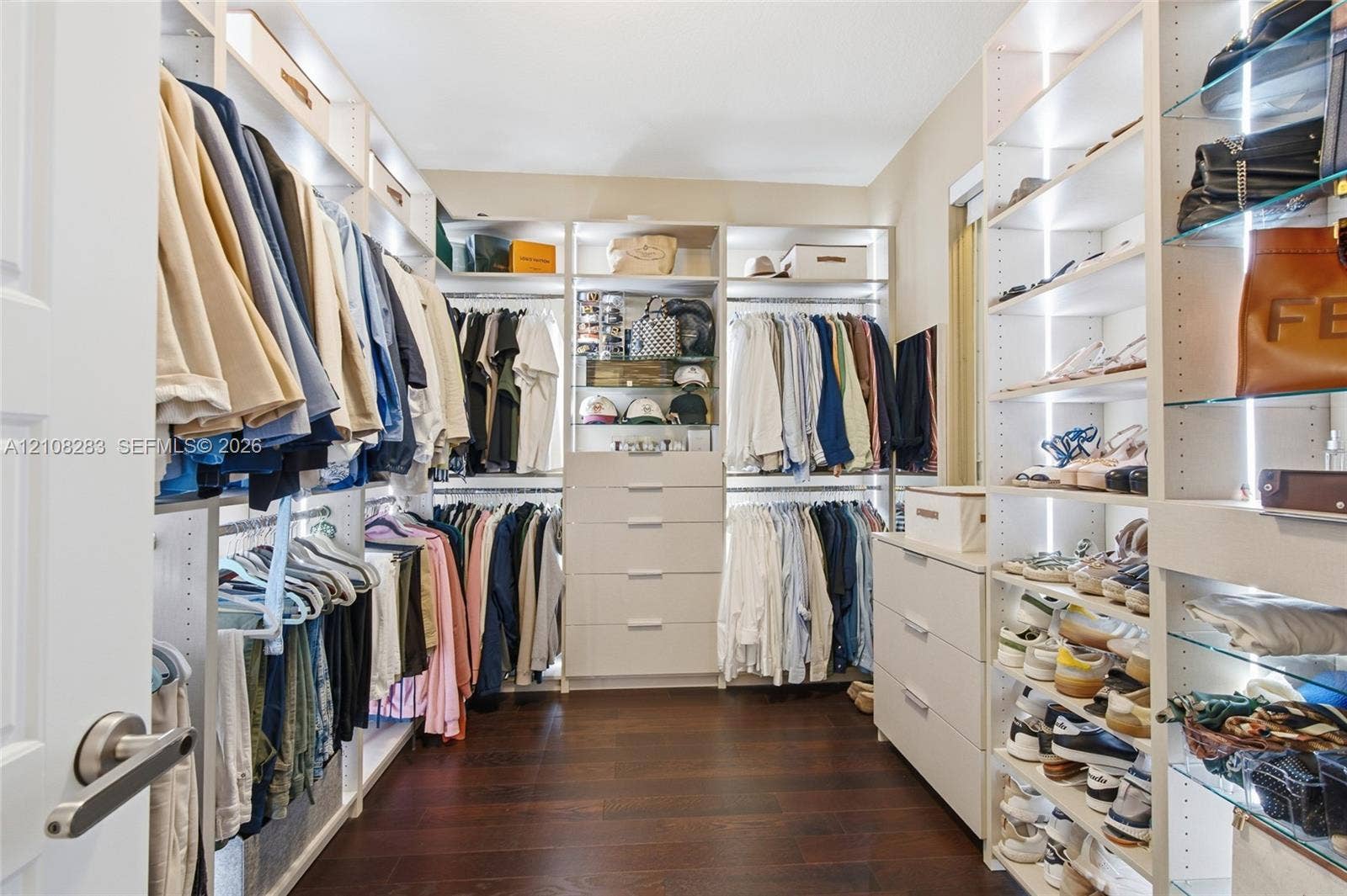 15215 SW 176th Lane, Miami, FL 33187 Walk-in closet featuring floor-to-ceiling custom built-in shelving, glass display shelving with integrated lighting, multi-tiered hanging rods, and integrated drawer units, all set upon dark wood-finish flooring