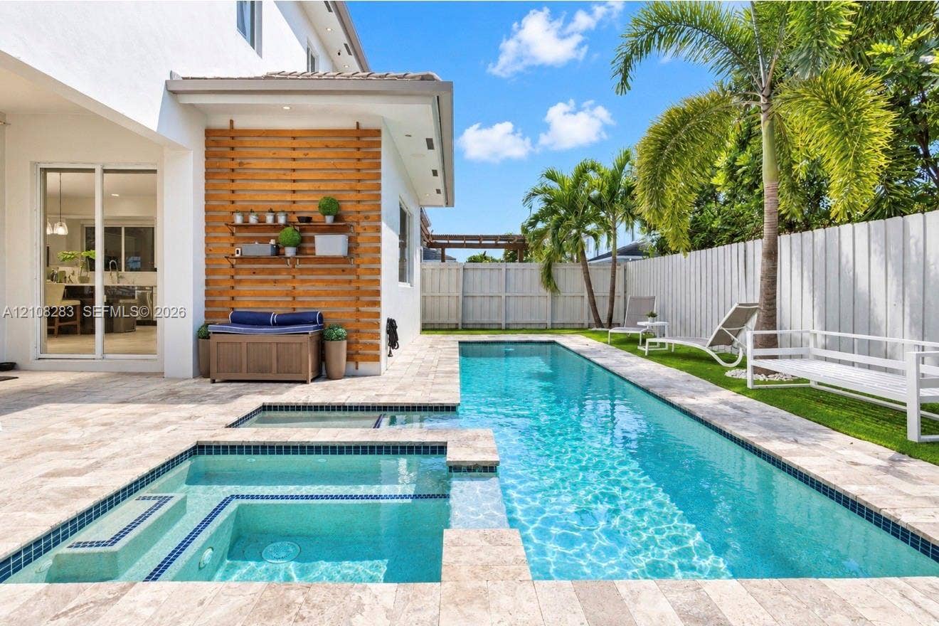 15215 SW 176th Lane, Miami, FL 33187 Custom pool with integrated spa featuring stone-tiled decking, decorative wood-slat accent wall, and perimeter fencing