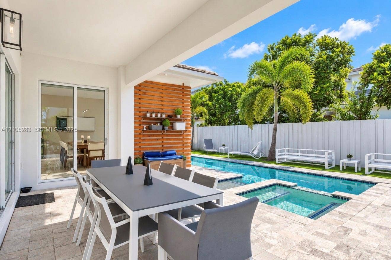 15215 SW 176th Lane, Miami, FL 33187 Covered patio featuring stone paver flooring, horizontal slat wood accent wall, built-in shelving, swimming pool with integrated spa, and vertical privacy fencing