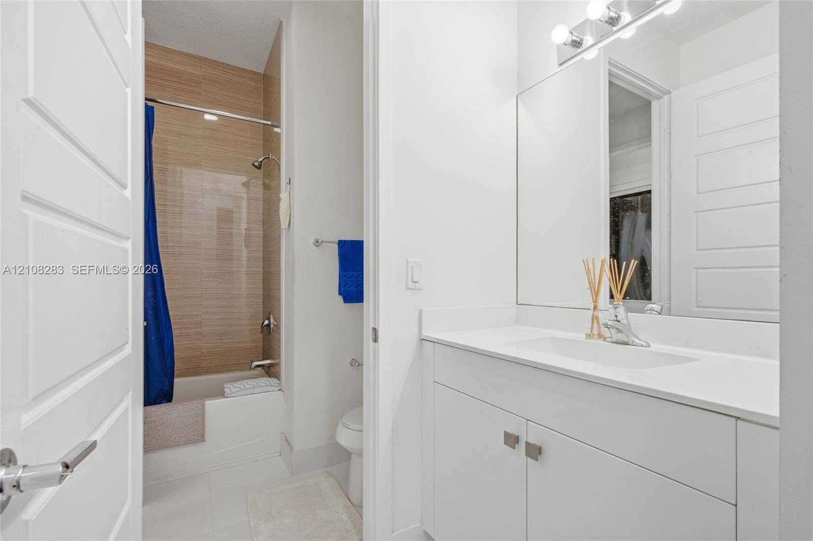 15215 SW 176th Lane, Miami, FL 33187 Bathroom featuring a white vanity with a composite countertop, an integrated rectangular sink, a floor-to-ceiling tiled shower surround with a light wood-finish pattern, and a wall-mounted light fixture above a large mirror
