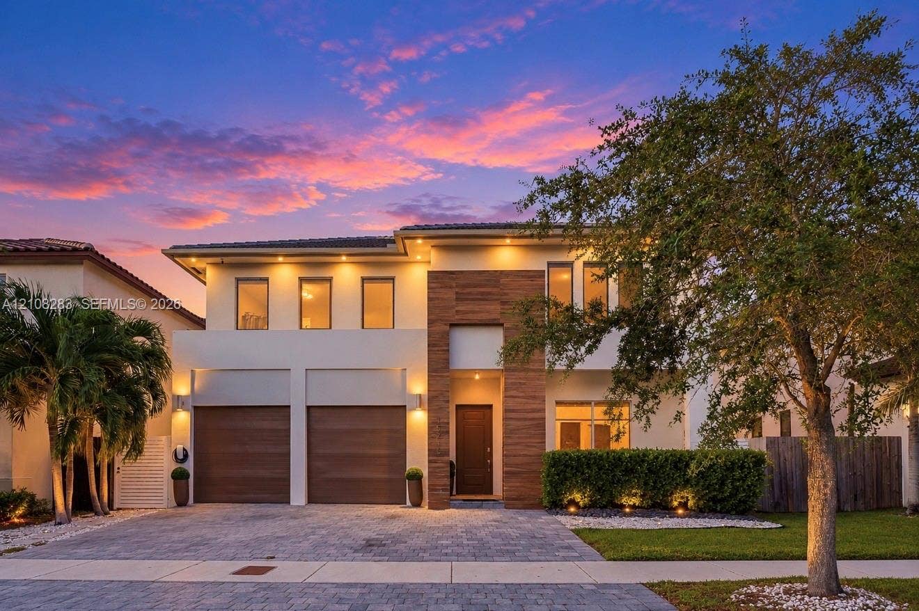 15215 SW 176th Lane, Miami, FL 33187 Two-story contemporary exterior featuring a light-toned stucco facade, wood-finish accents, integrated soffit lighting, a two-car garage, and a paver driveway