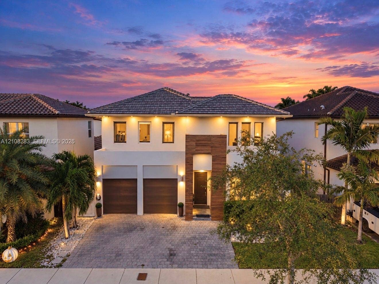 15215 SW 176th Lane, Miami, FL 33187 Two-story residence featuring a paved driveway, dual-car garage with wood-finish doors, contemporary tile roof, and textured stone facade accents