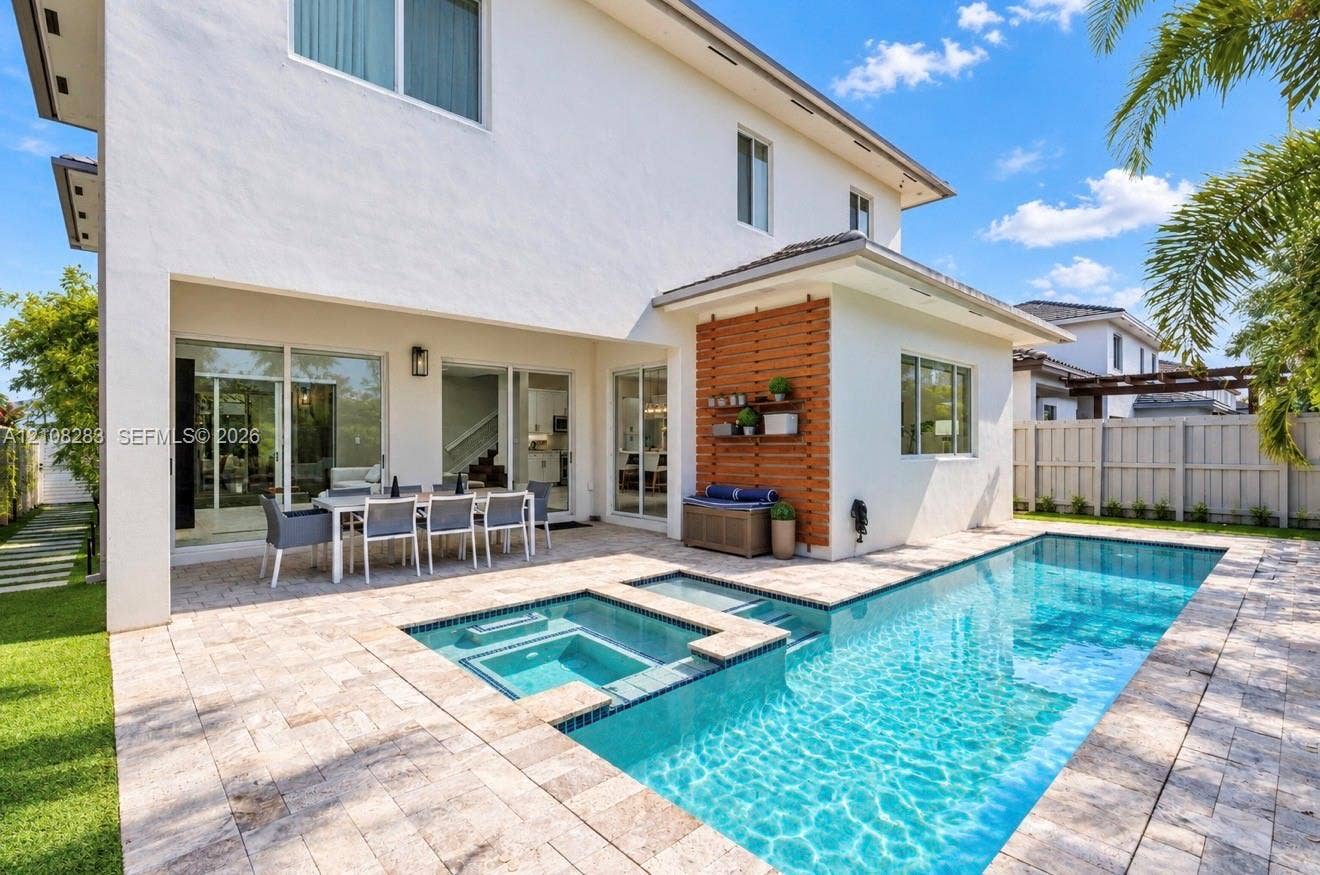 15215 SW 176th Lane, Miami, FL 33187 Backyard featuring an in-ground swimming pool, integrated spa, stone paver decking, white exterior siding, and vertical wood-slat accent wall