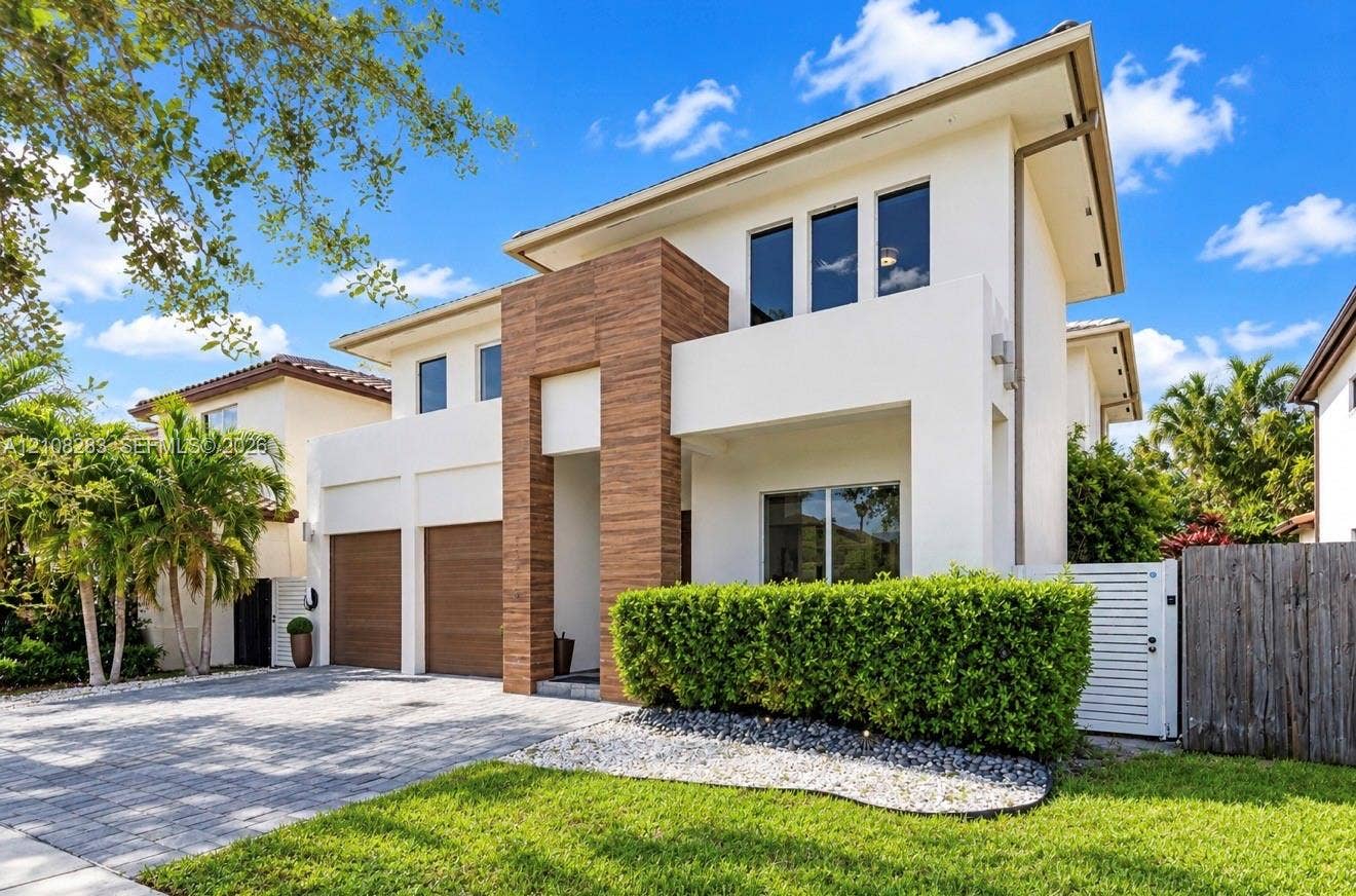 15215 SW 176th Lane, Miami, FL 33187 Modern two-story exterior featuring a smooth stucco finish, wood-tone architectural detailing, a paver driveway, and a double-car garage