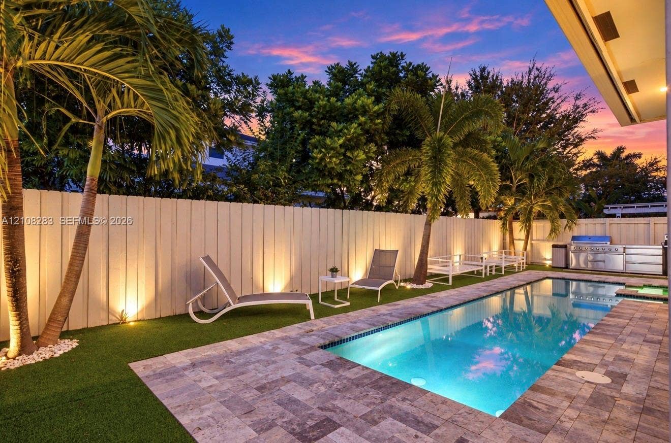 15215 SW 176th Lane, Miami, FL 33187 Backyard featuring a rectangular swimming pool, stone-paver decking, integrated outdoor kitchen, artificial turf, and perimeter wall lighting
