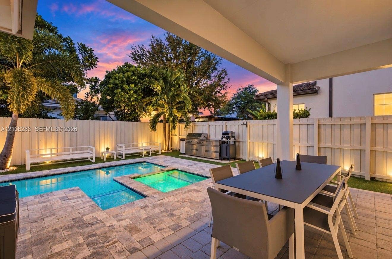 15215 SW 176th Lane, Miami, FL 33187 Covered patio featuring stone-paver decking, integrated swimming pool with inset spa, built-in stainless steel outdoor kitchen, and perimeter privacy fencing