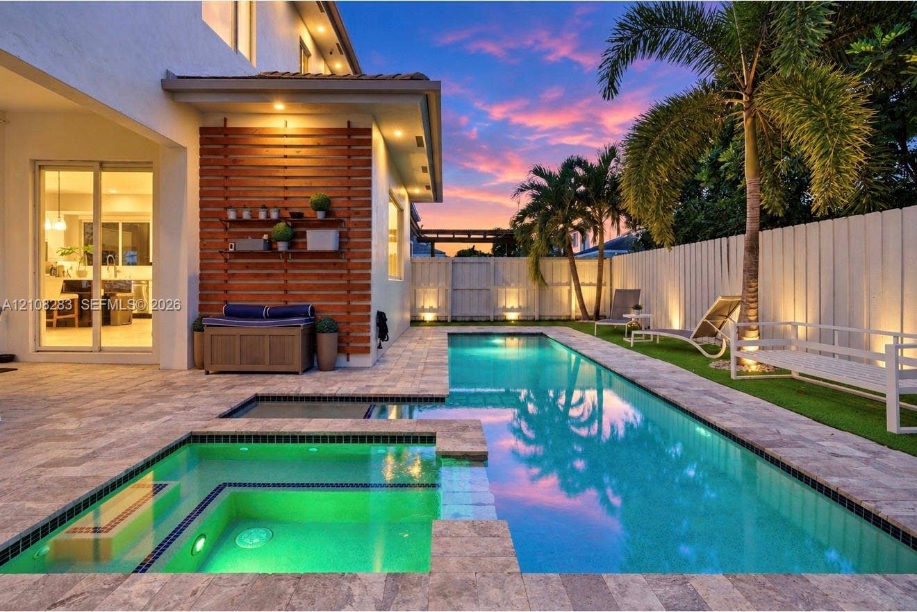 15215 SW 176th Lane, Miami, FL 33187 Outdoor living area featuring a rectangular swimming pool with an integrated spa, stone paver decking, horizontal wood-slat accent wall, and perimeter privacy fencing