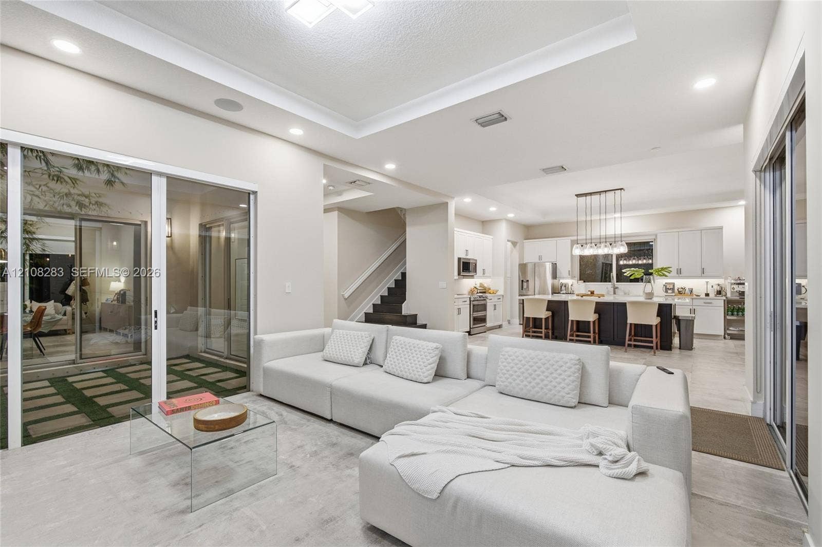 15215 SW 176th Lane, Miami, FL 33187 Open-concept living space featuring a tray ceiling, recessed lighting, large sliding glass doors, neutral tile flooring, and a kitchen with an oversized island and white cabinetry