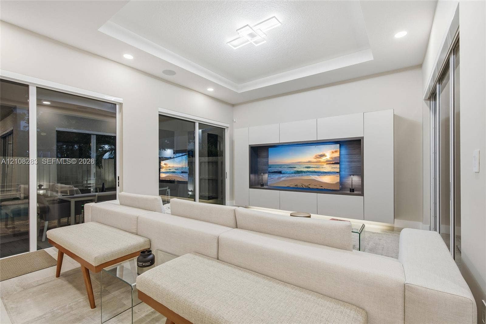15215 SW 176th Lane, Miami, FL 33187 Tray ceiling with integrated geometric lighting, large-format tile flooring, and custom built-in cabinetry featuring recessed media display with wood-toned back paneling and under-cabinet illumination