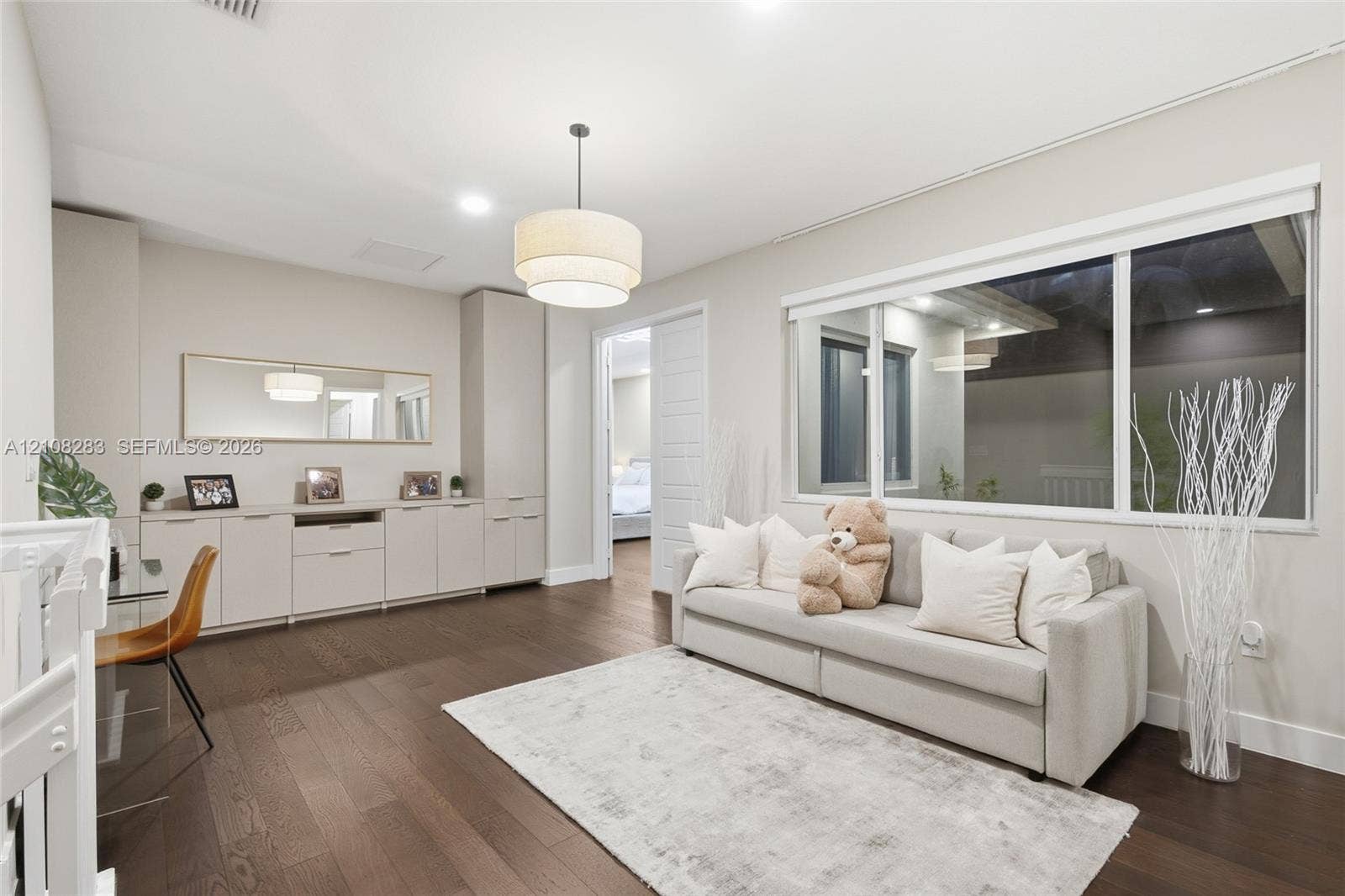 15215 SW 176th Lane, Miami, FL 33187 Spacious room featuring wood-finish flooring, extensive built-in cabinetry, a modern tiered drum pendant light, and a large horizontal window