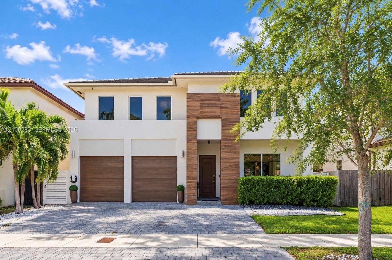 15215 SW 176th Lane, Miami, FL 33187 Two-story exterior featuring light-toned stucco, wood-finish accents, a paver driveway, and an attached two-car garage