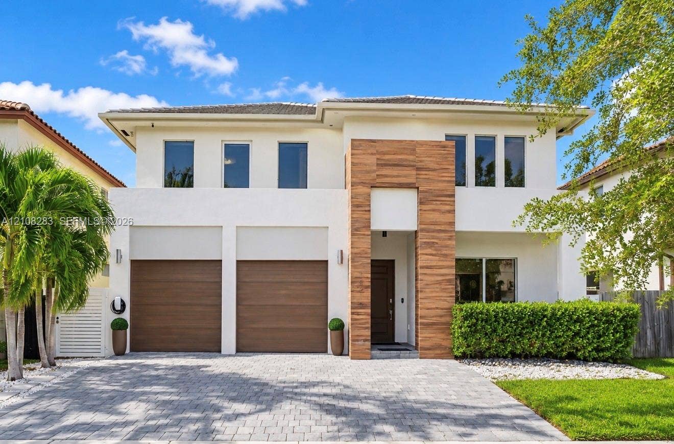 15215 SW 176th Lane, Miami, FL 33187 Two-story exterior featuring smooth stucco finish, vertical wood-plank architectural cladding, paver driveway, and dual wood-finish garage doors