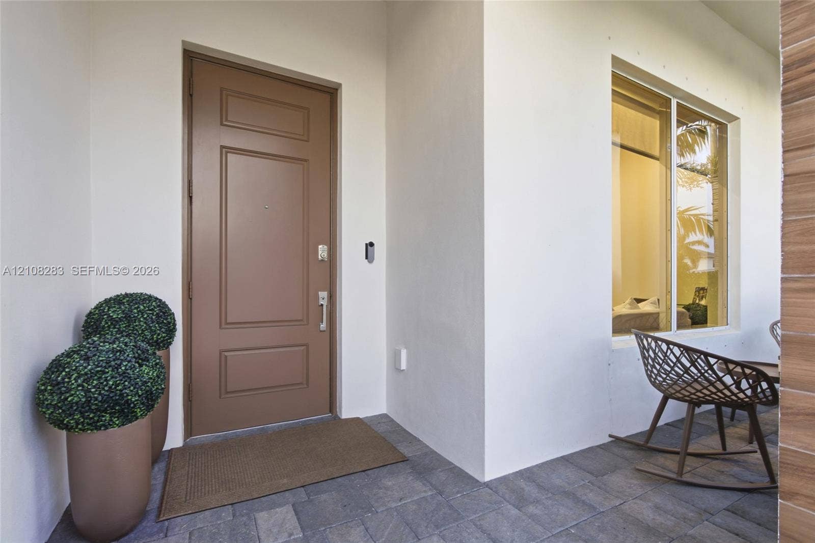 15215 SW 176th Lane, Miami, FL 33187 Covered entryway featuring a solid-panel door, stone paver flooring, recessed exterior lighting, and a large picture window