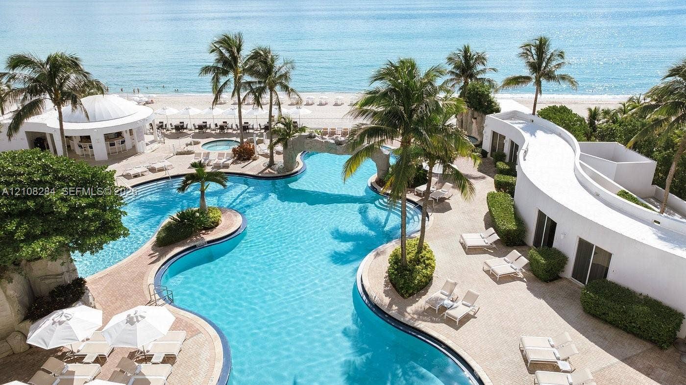 18001 Collins Avenue, #908, Sunny Isles Beach, FL 33160 Freeform swimming pool with integrated rock features, surrounding paved deck, palm tree landscaping, and direct beach access